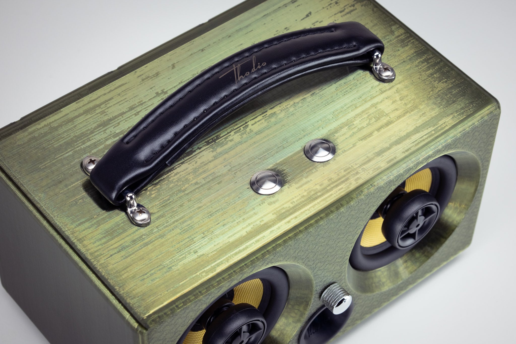 Detail of the padded leather carry handle and stainless steel control buttons on top of the emerald green Thodio 3D-printed speaker