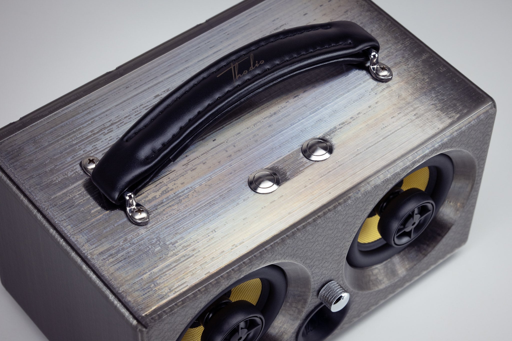 Detail of the leather carry handle and chrome control buttons on top of the grey iBox Mini 3D-printed speaker