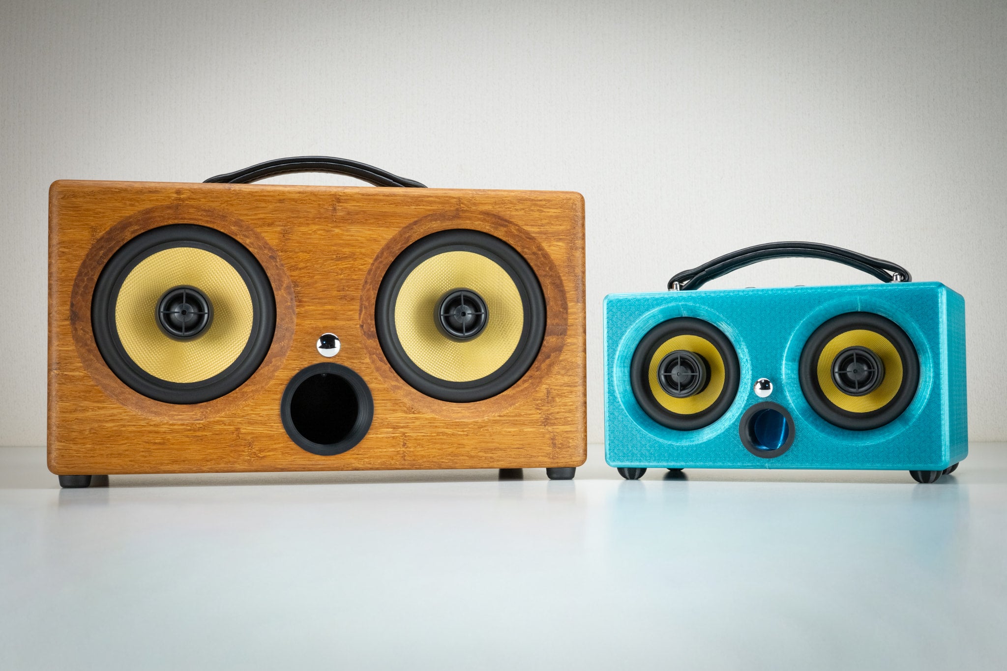 Turquoise Thodio iBox Mini 3D-printed speaker next to the larger handmade bamboo iBox XC, showing size comparison