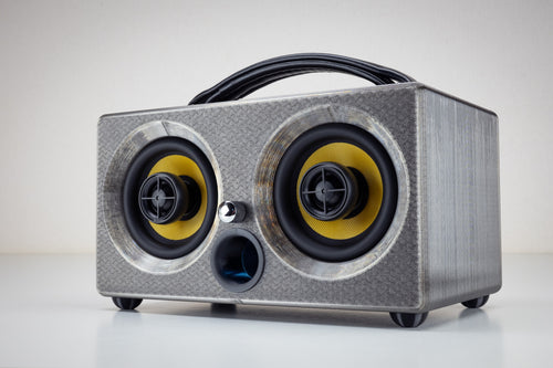 Grey gunmetal Thodio iBox Mini 3D-printed Bluetooth speaker, front three-quarter view with twin coaxial drivers and leather handle