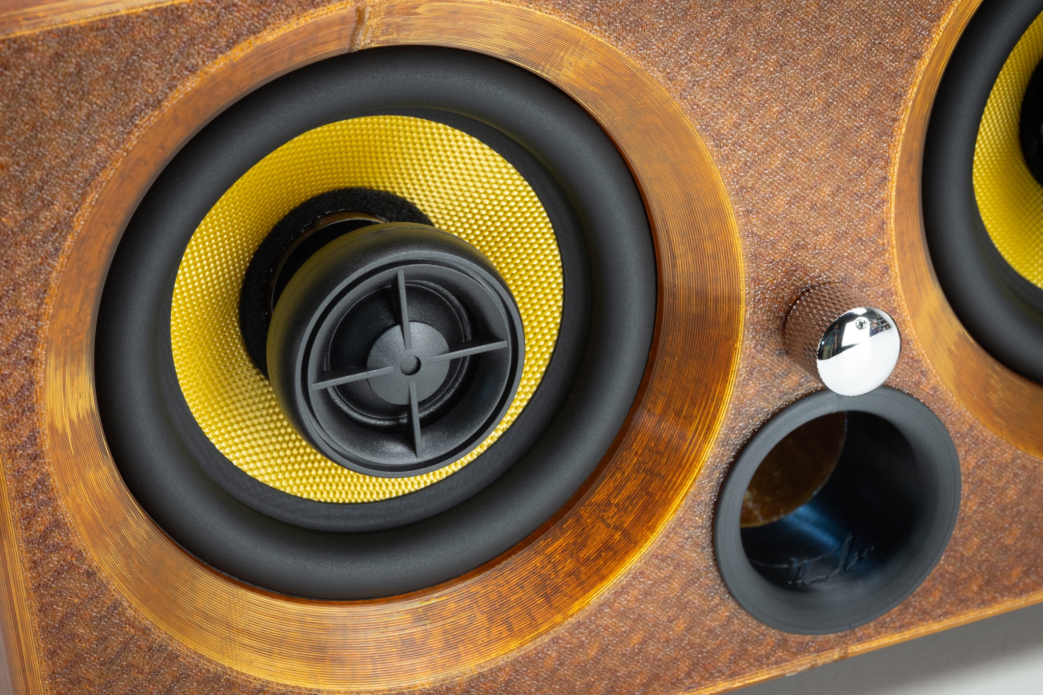Macro detail of the amber Thodio iBox Mini driver showing the Kevlar coaxial cone, silk-dome tweeter and bass-reflex port