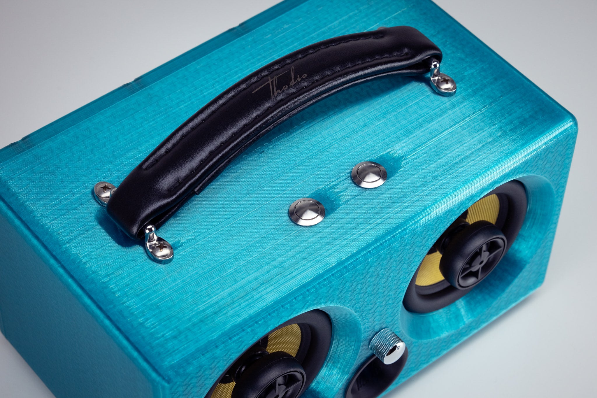 Detail of the leather carry handle and chrome control buttons on top of the turquoise iBox Mini 3D-printed speaker